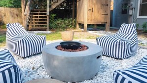 Eine Terrasse mit zwei gestreiften Liegesesseln, einer runden Feuerstelle und einem Holzdeck mit Treppe.