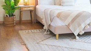 Ein Schlafzimmer mit einem Bett, einem wandmontierten runden Spiegel, einem Blumentopf, einem kleinen Tisch mit einer Lampe und einem großen Teppich.