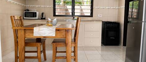 Una cocina con una mesa de comedor, sillas, microondas, estufa y refrigerador.