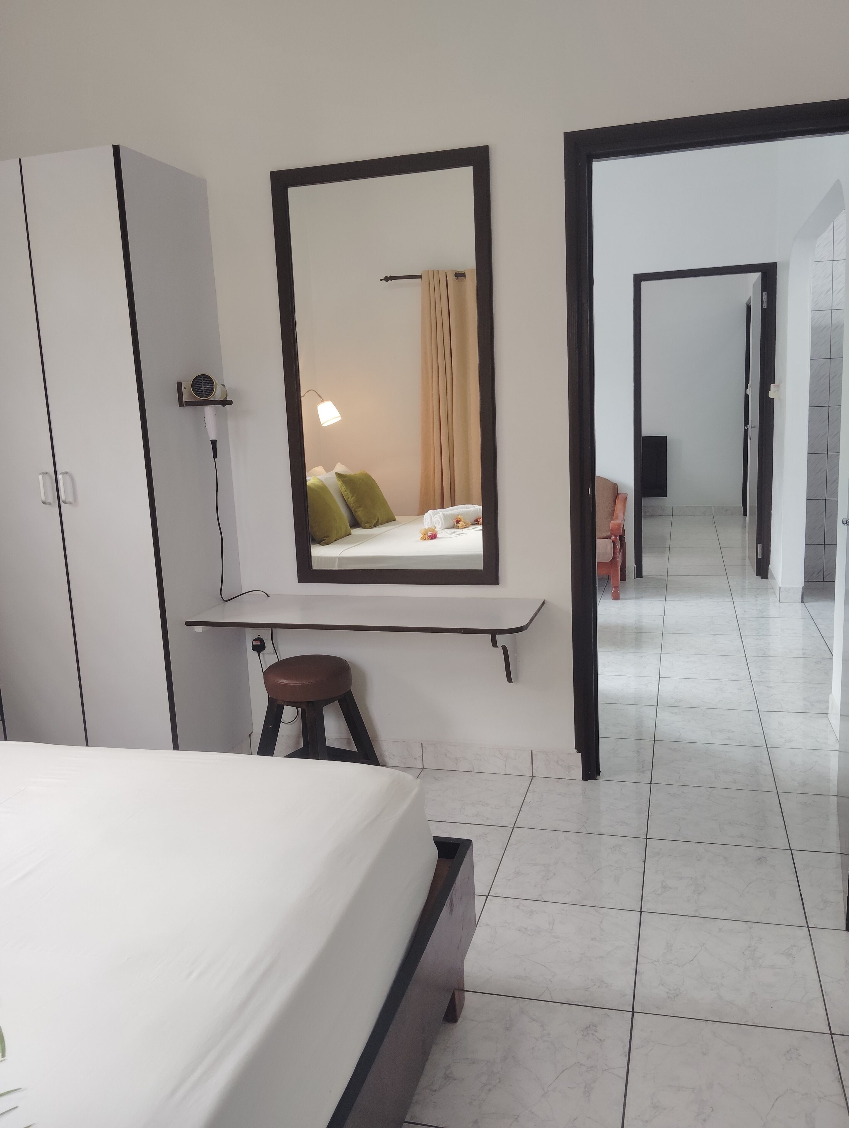 A hotel room with a bed, a desk with a mirror, a chair, and a bathroom visible through an open door.