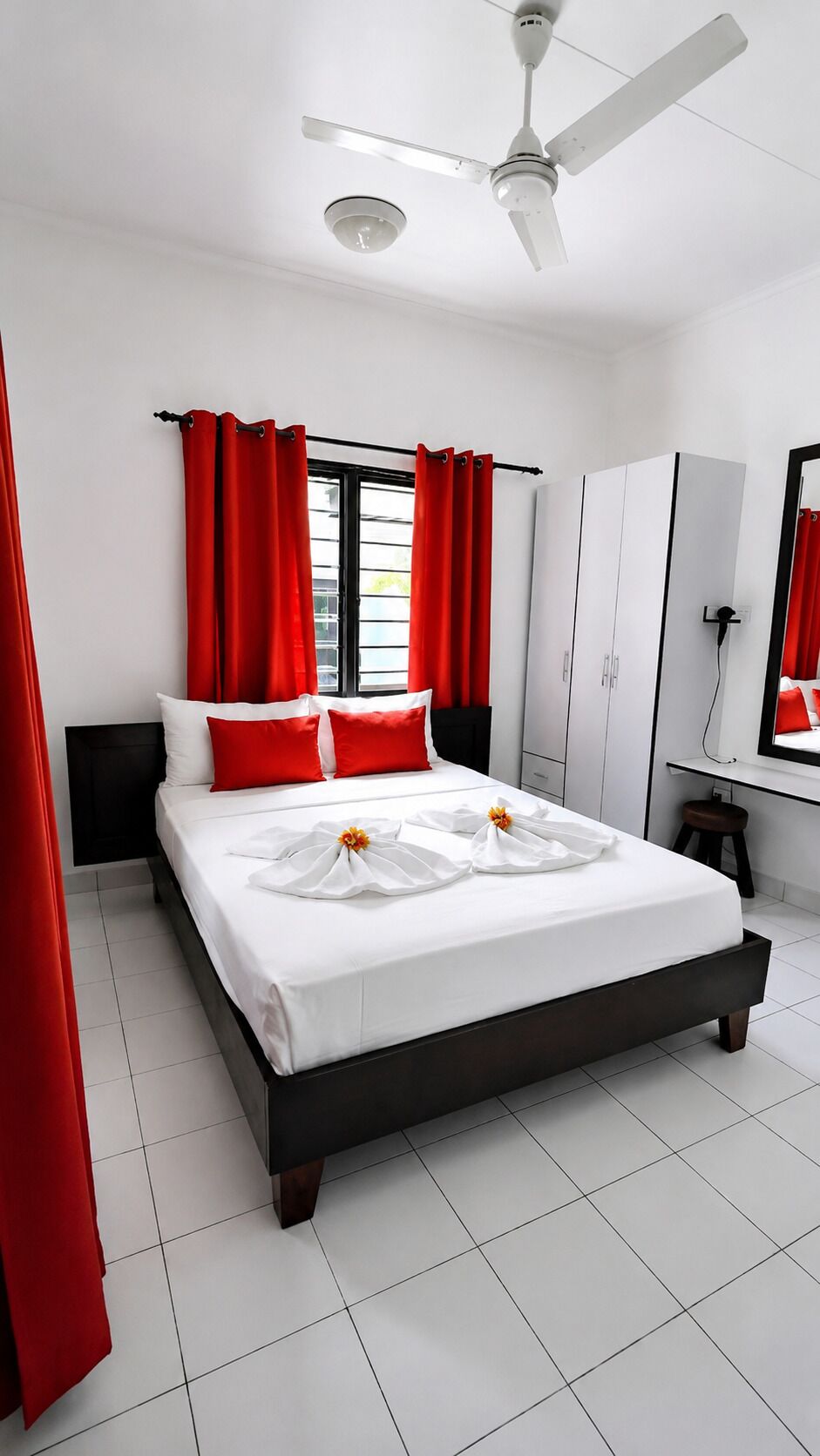 Una habitación de hotel con cama, cortinas rojas, ventilador de techo y escritorio con espejo.