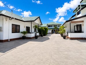 A courtyard with two-story buildings, potted plants, and a clear sky. - Roche Kerlan Apartments (Praslin Island)