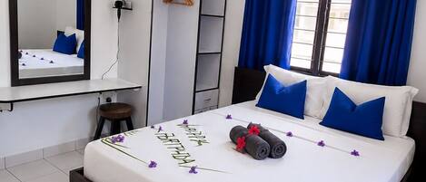 A bedroom with a bed, a wardrobe, a mirror, a ceiling fan, and a window with curtains.