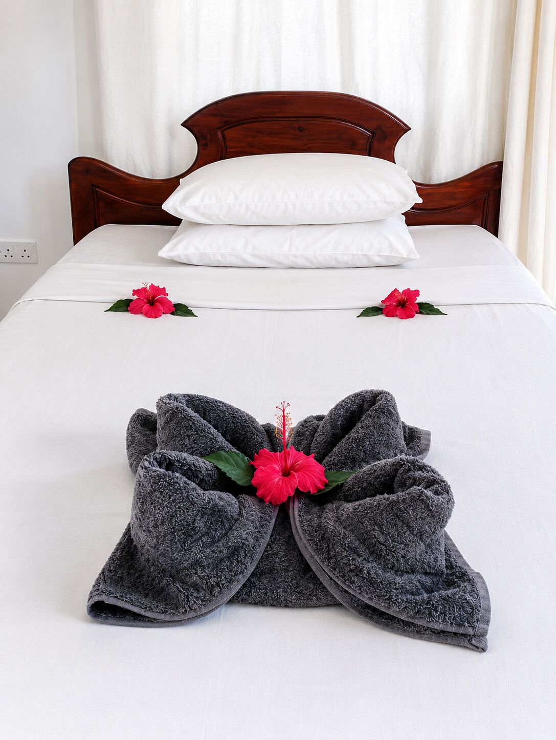 A neatly made bed with white linens, two pillows, and a towel arrangement with a hibiscus flower.