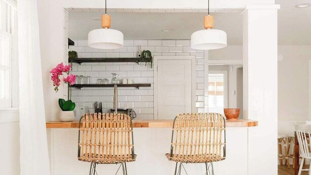 A kitchen with white cabinets, two bar stools, pendant lights, and a wooden countertop.