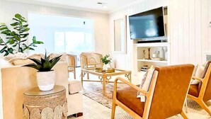 Un salon moderne avec un canapé, des fauteuils, une table basse, un téléviseur et une grande fenêtre.