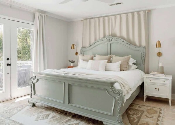 Une chambre à coucher avec un lit, des tables de chevet et une vue sur l’extérieur, visible à travers une porte.