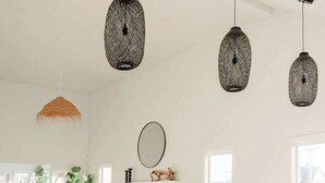 A spacious living room with a white sofa set, a wooden bench, and a round coffee table. There are three hanging pendant lights and a large mirror on the wall.