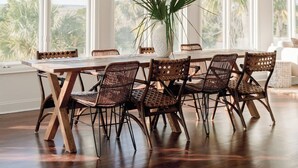 A dining area with a wooden table and wicker chairs, large windows, and a ceiling fan.