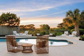 A poolside area with wicker chairs and a table, surrounded by palm trees and a wooden fence. - Marshfront 5BD Oasis | Pool, Yard & Steps to Beach (Folly Beach)