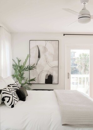 A bedroom with a bed, a ceiling fan, a large abstract painting, and a view through a door. - Marshfront 5BD Oasis | Pool, Yard & Steps to Beach (Folly Beach)
