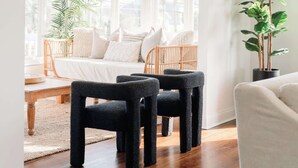 A bright room with a wooden floor, a white sofa, a black armchair, and a large window.