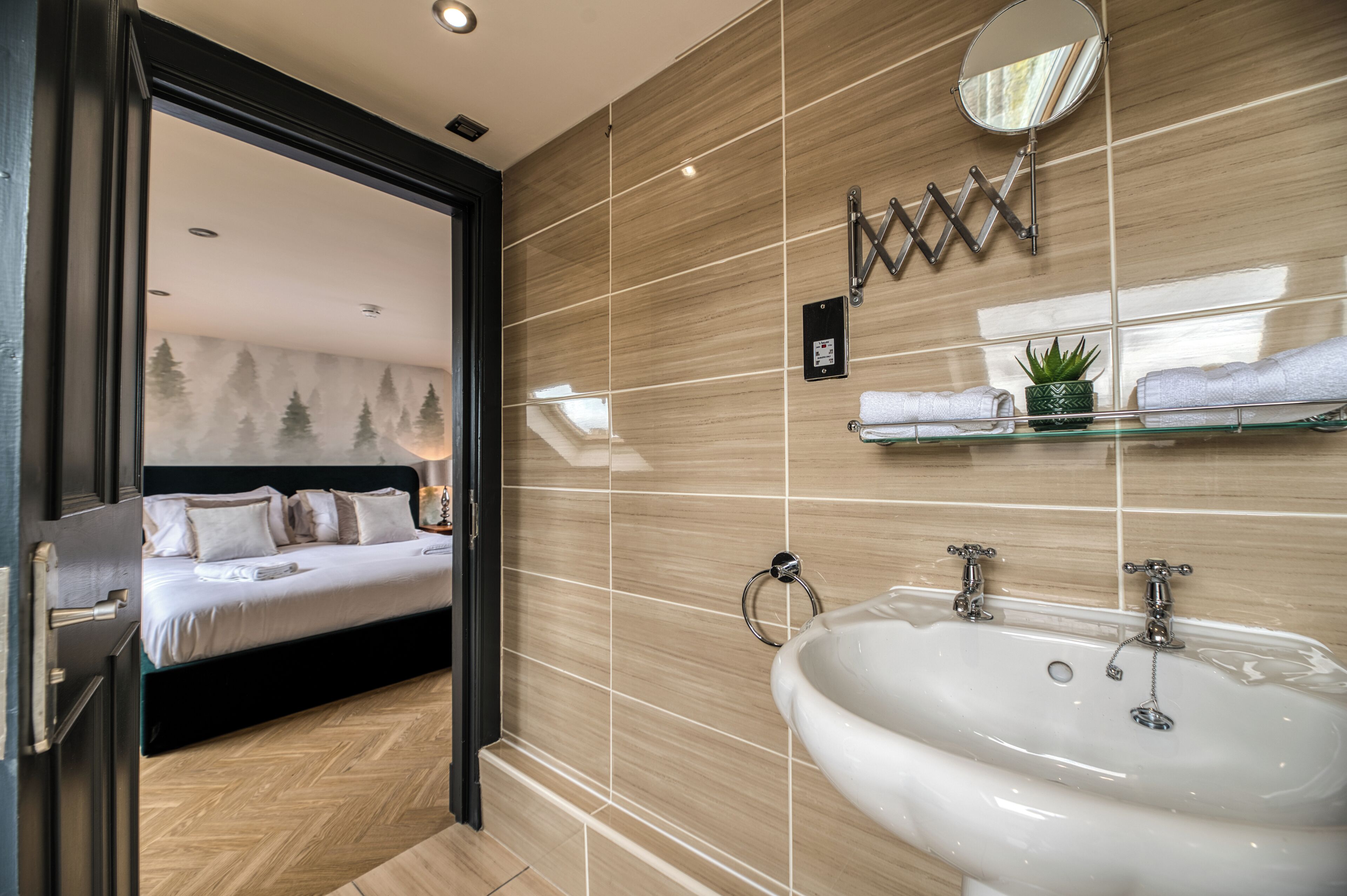 Ein modernes Hotelzimmer mit einem großen Bett, einem Badezimmer mit Waschbecken und Spiegel sowie einem Holzboden.
