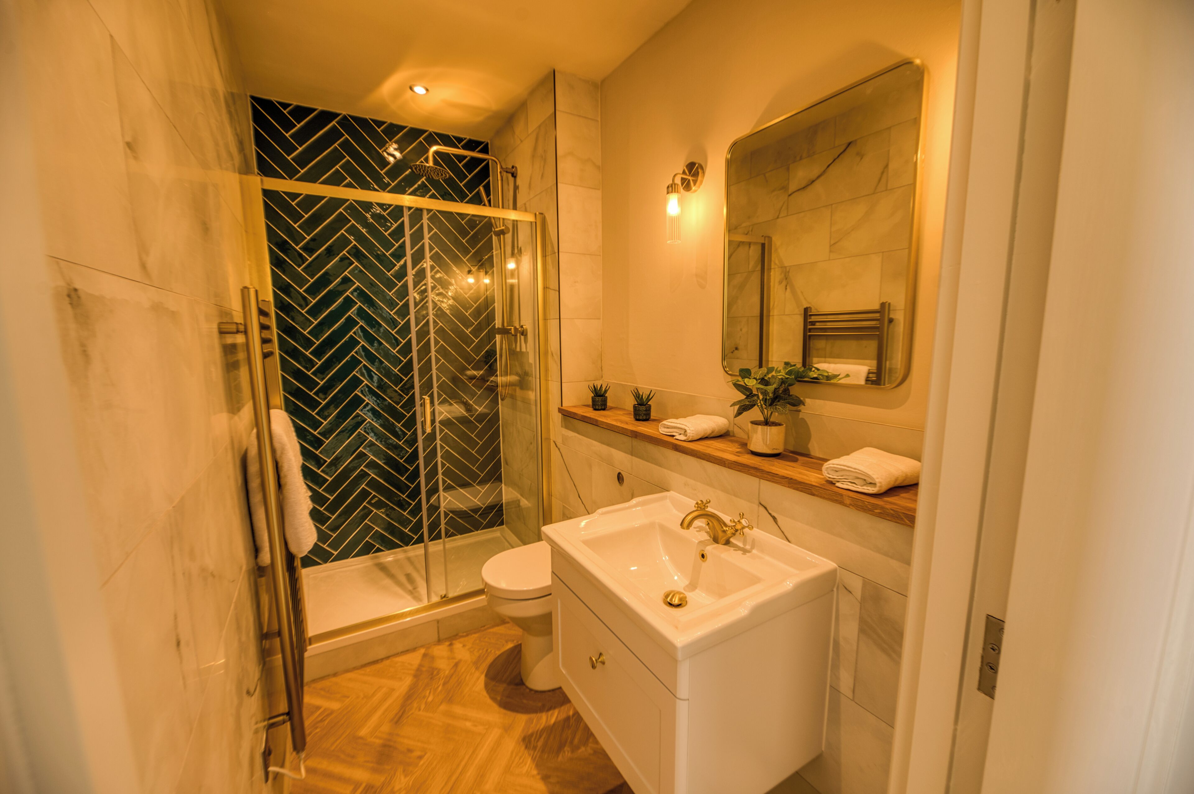 Un baño moderno con ducha envuelta en vidrio, lavabo blanco y zona de ducha con azulejos de mármol.