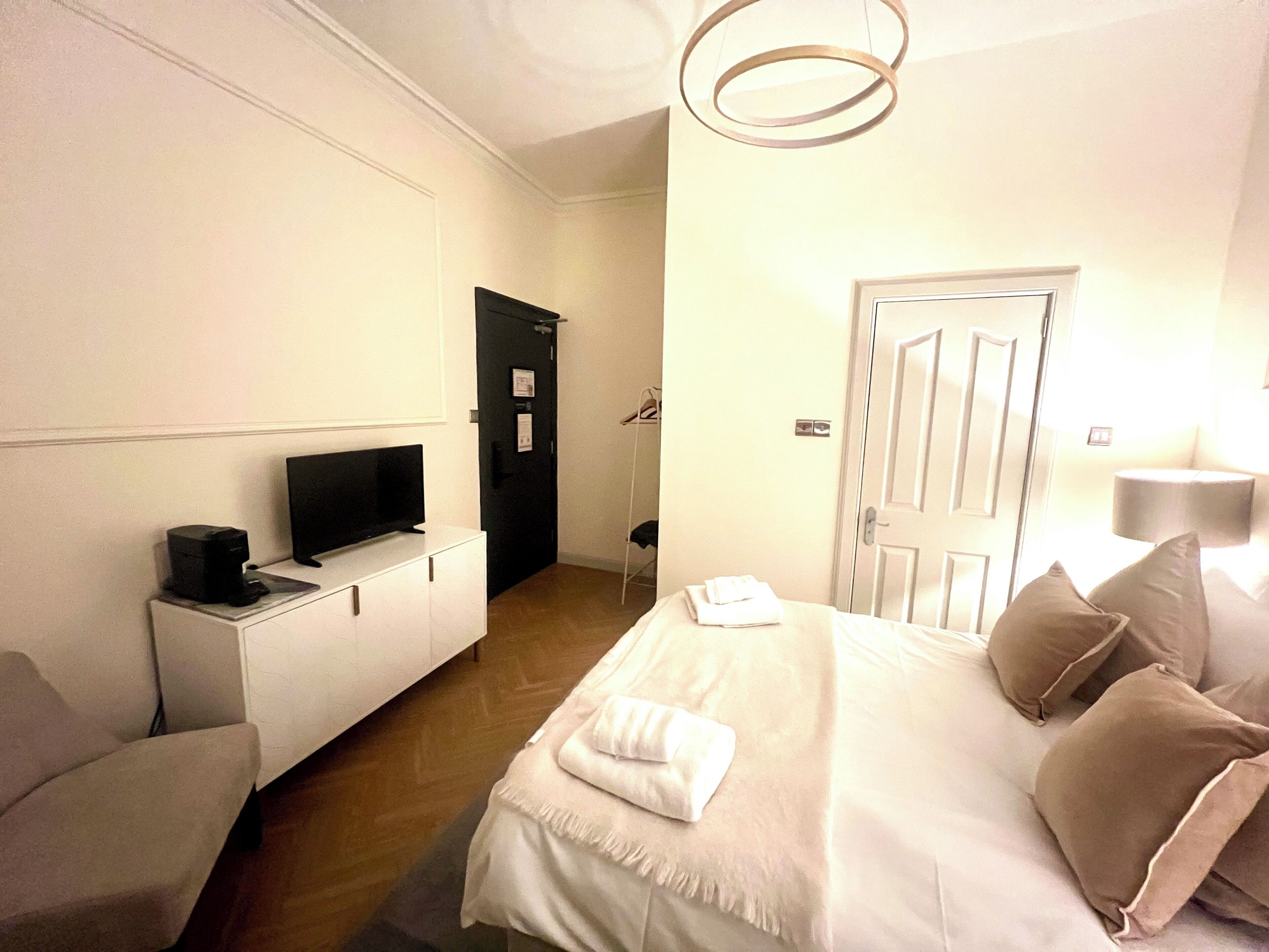 A hotel room with a bed, a TV on a bedside table, a door, and a lamp.