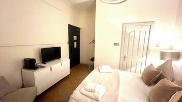 A hotel room with a bed, a TV on a bedside table, a door, and a lamp.