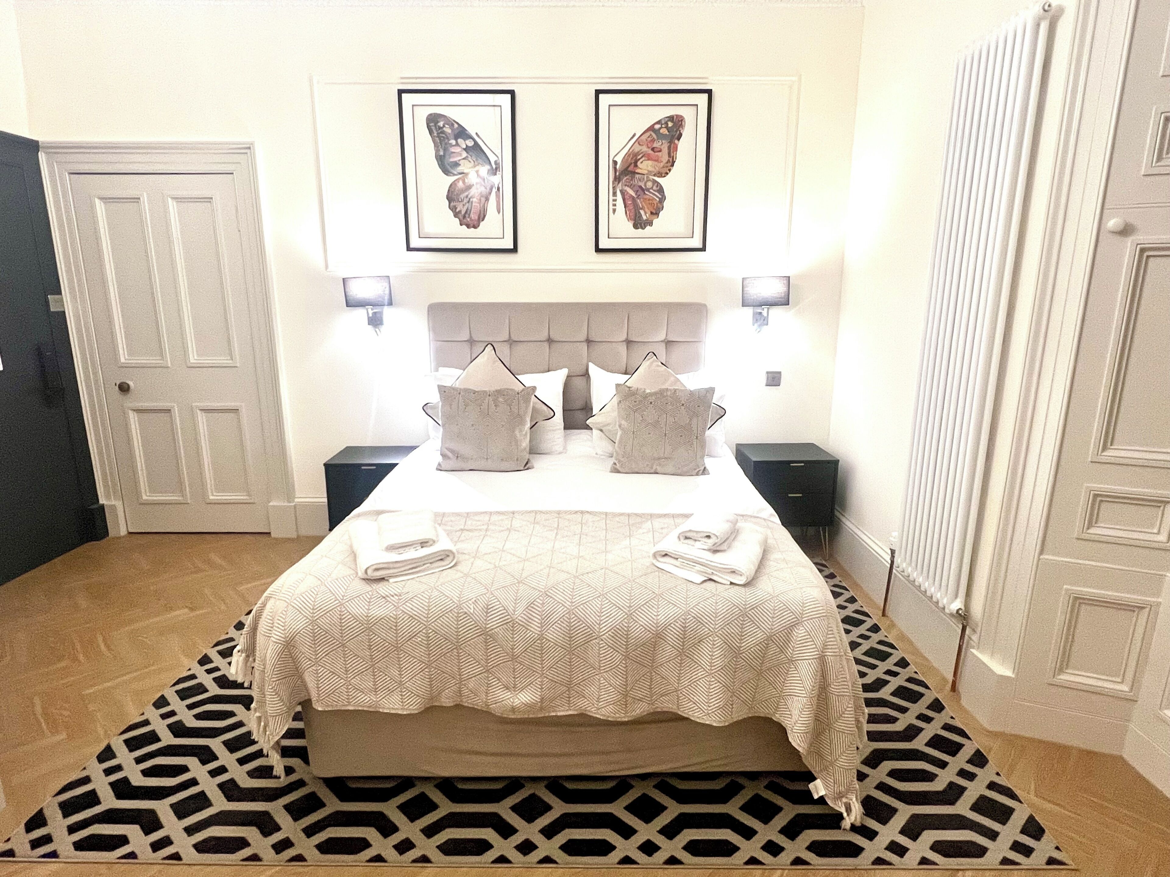 Hotelkamer met een bed, twee nachtkastjes, een hoofdeinde, een kamerkleed en twee foto’s in lijsten aan de muur.