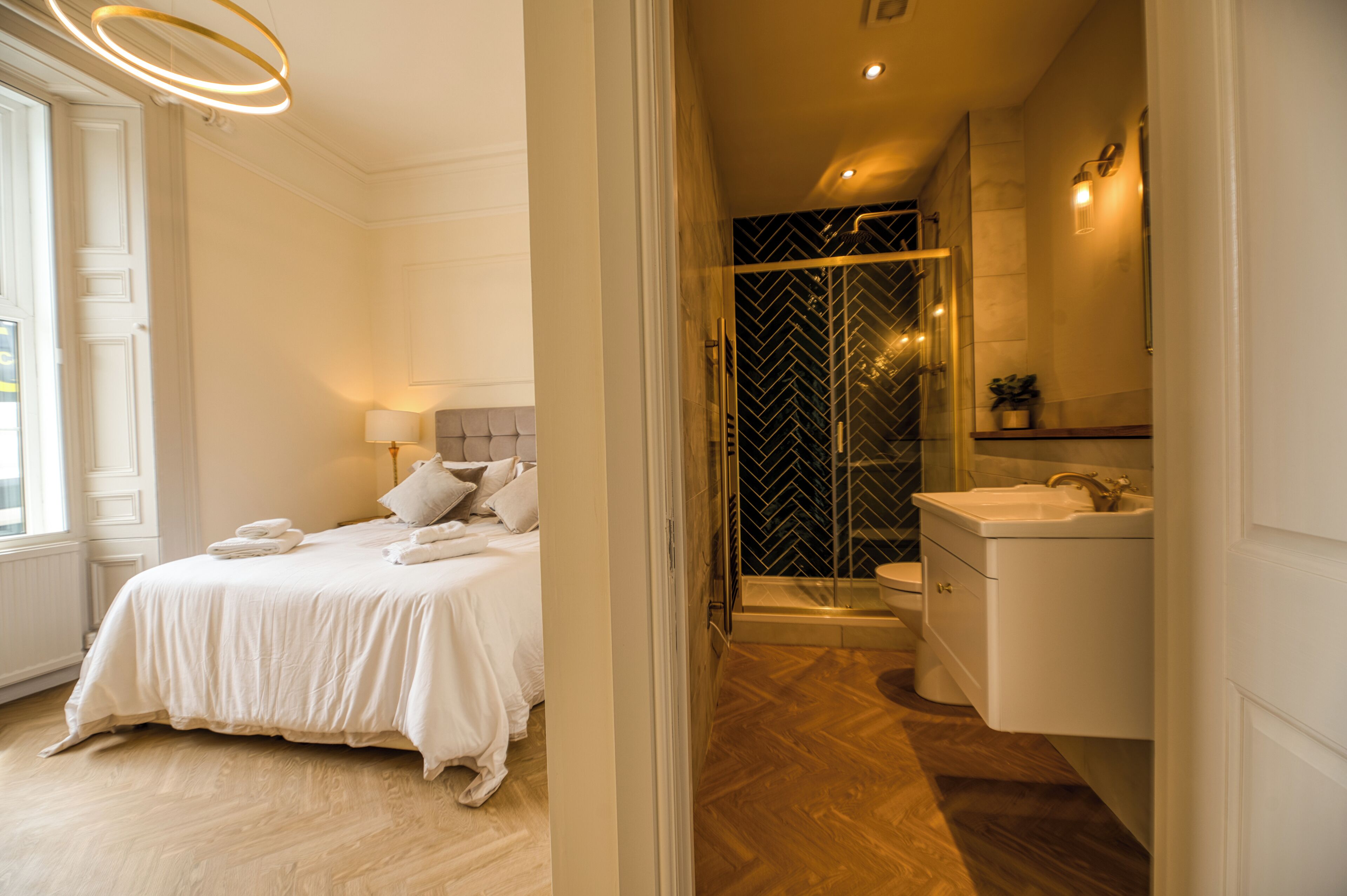 A modern bedroom with a large bed, a bedside table, and a nightstand. There is a bathroom with a shower, a sink, and a toilet.