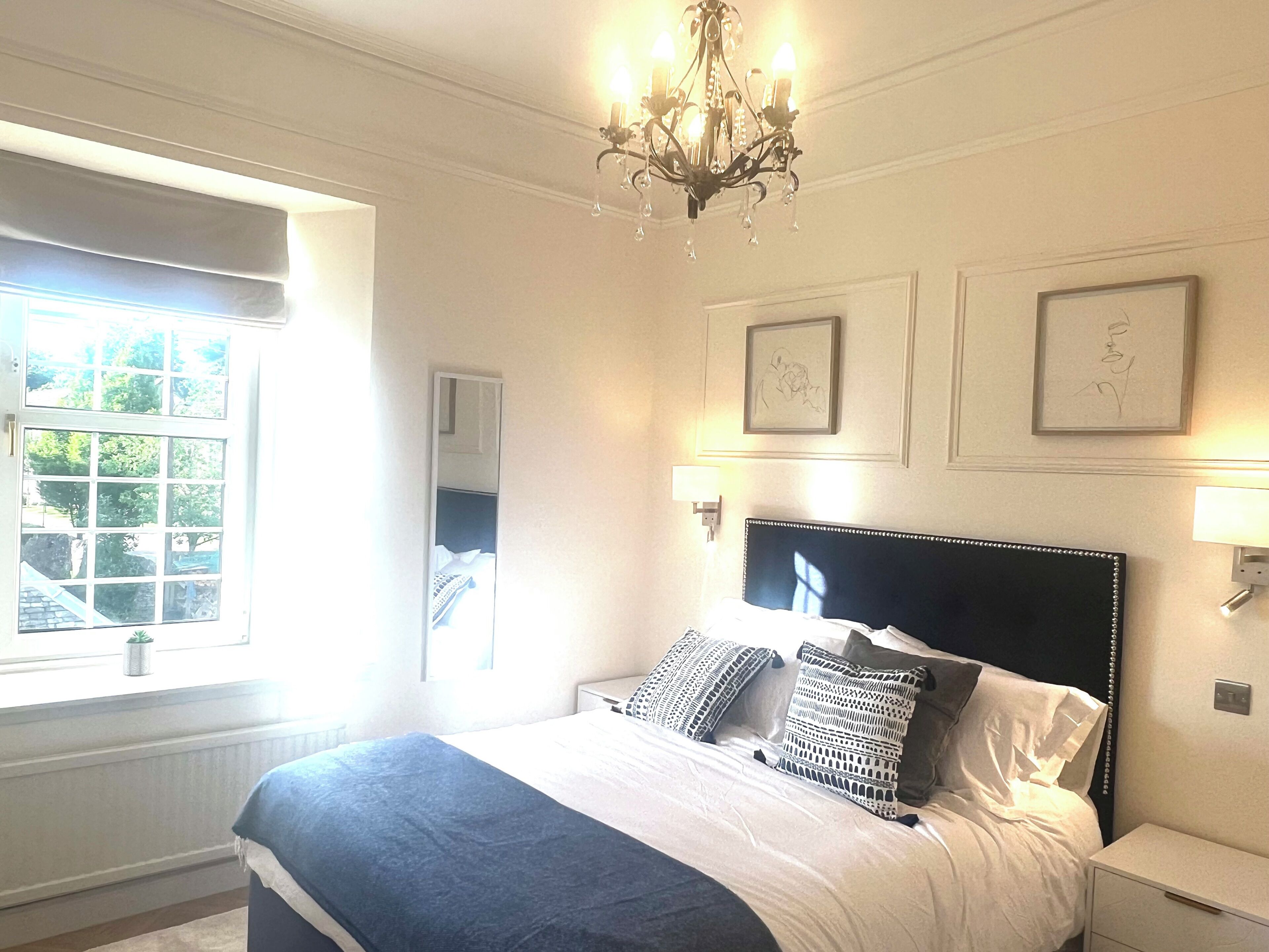 Une chambre à coucher avec un grand lit, des lampes de chevet, un lustre et des œuvres d’art encadrées accrochées au mur.