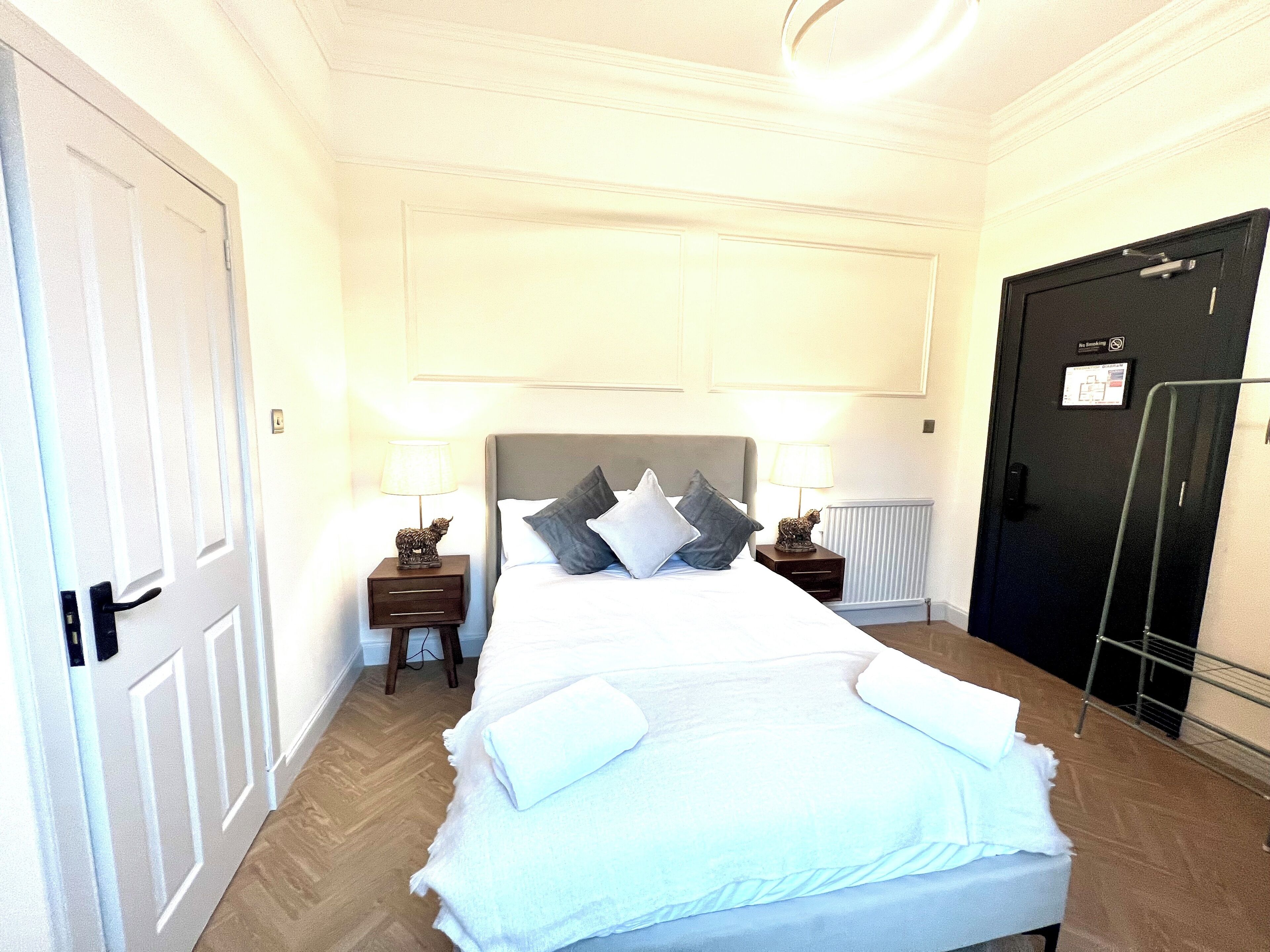 A hotel room with a bed, two bedside tables with lamps, a radiator, and a door with a sign.