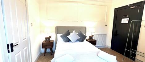 A hotel room with a bed, two bedside tables with lamps, a radiator, and a door with a sign.