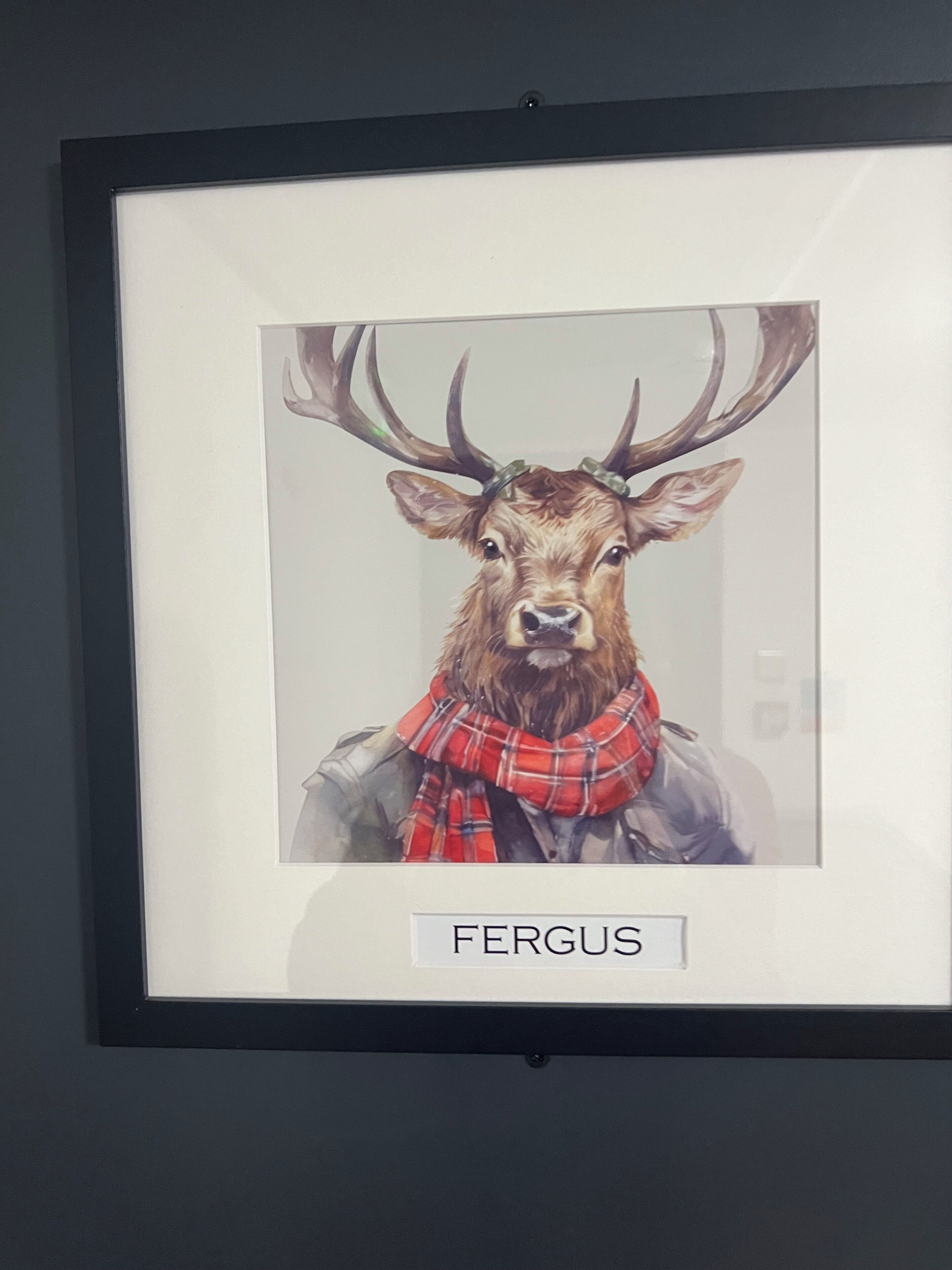 Una obra de arte en marco que muestra un ciervo con astas y una bufanda escocesa roja, con el texto 'FERGUS'.