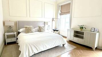 A bedroom with a bed, bedside tables, a dresser, a hanging light fixture, and a window with a view.