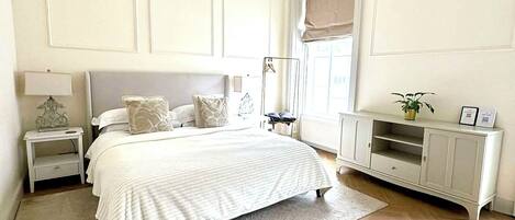 Un dormitorio con cama, mesitas de noche, cómoda, lámpara colgante y ventana con vistas.