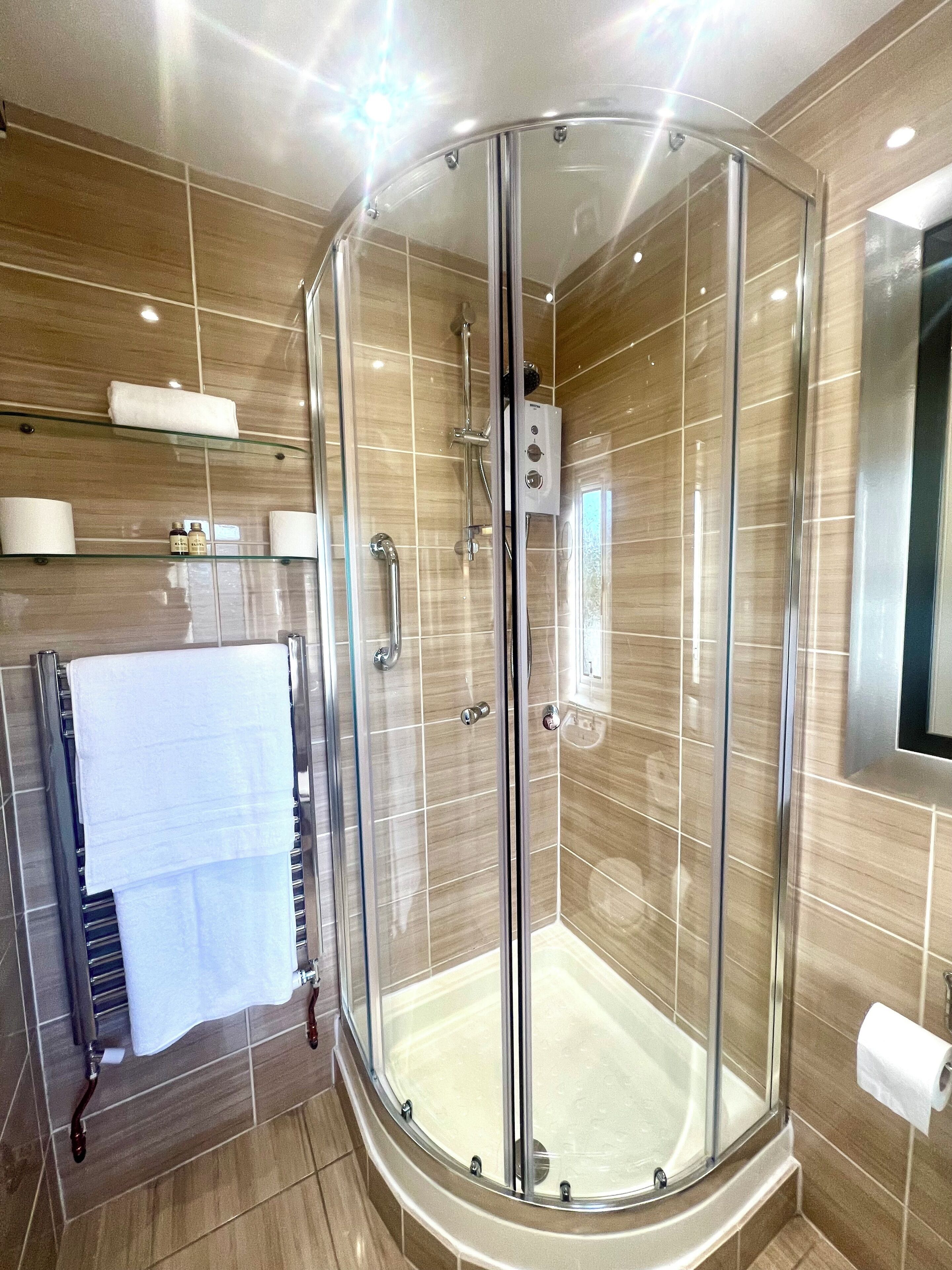 A glass-enclosed shower stall with a bathtub, a towel rack with towels, and a toilet paper holder.