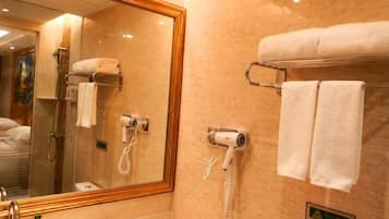Un baño de hotel con un espejo grande, un lavamanos, un perchero con dos toallas y un secador de pelo.