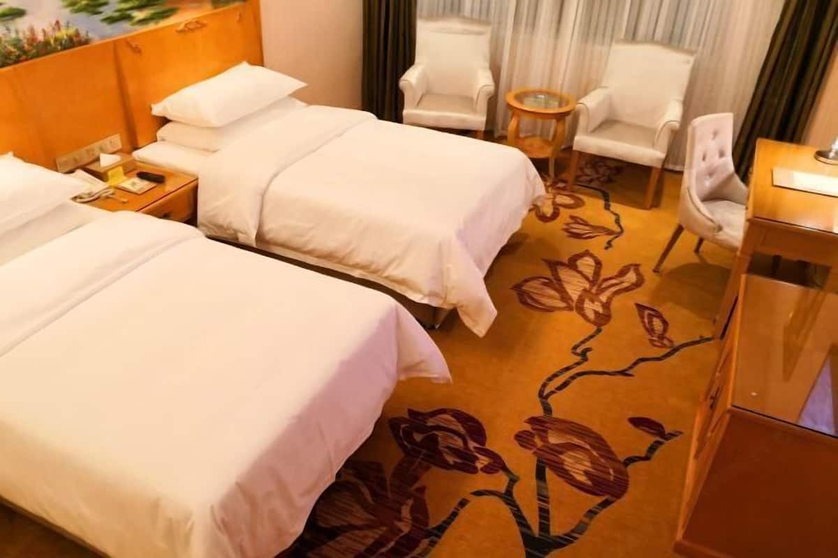 A hotel room with two beds, a small table, two chairs, and a carpet with a floral pattern.