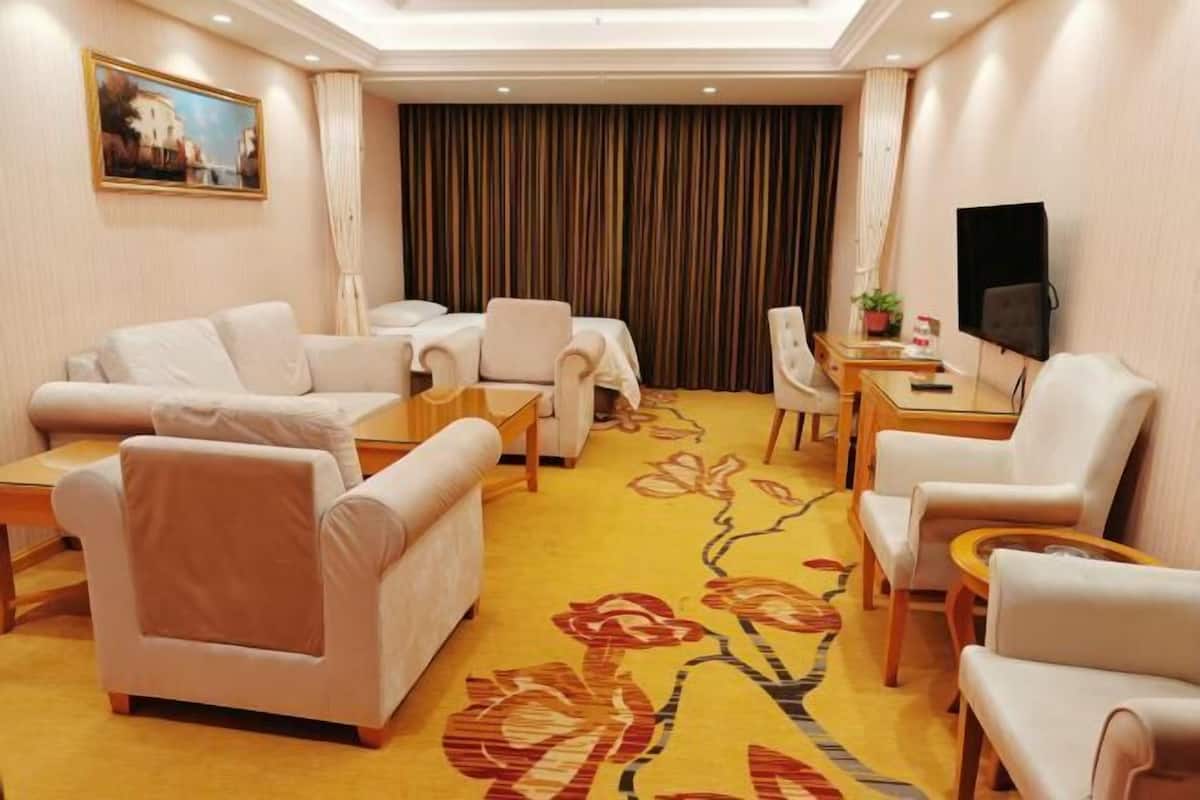 A hotel room with a sofa set, a dining table, a TV, and a carpet with floral patterns.
