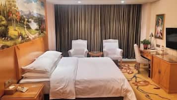 A hotel room with a large bed, two white armchairs, a desk with a chair, a television, and a painting on the wall.
