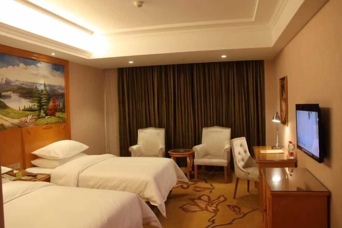 A hotel room with two beds, a desk, a TV, and a painting on the wall.