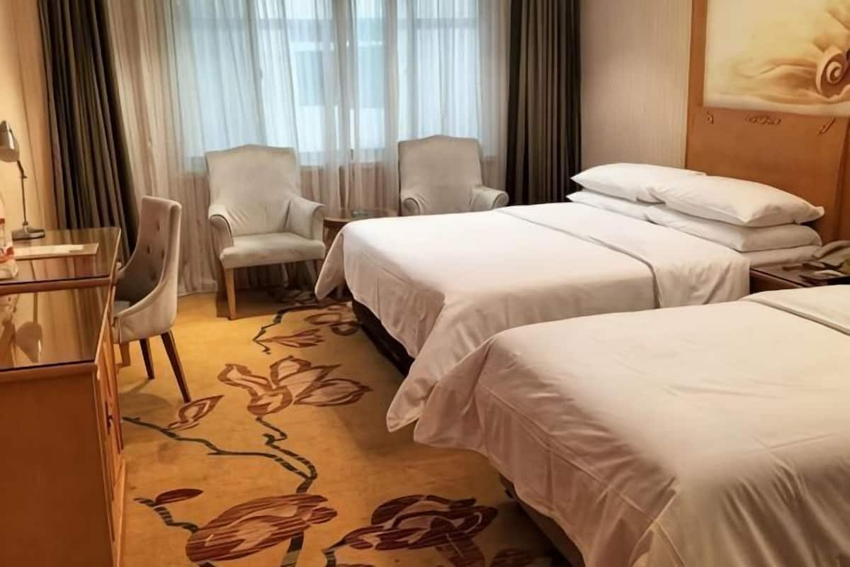 A hotel room with two beds, a desk, and two chairs.