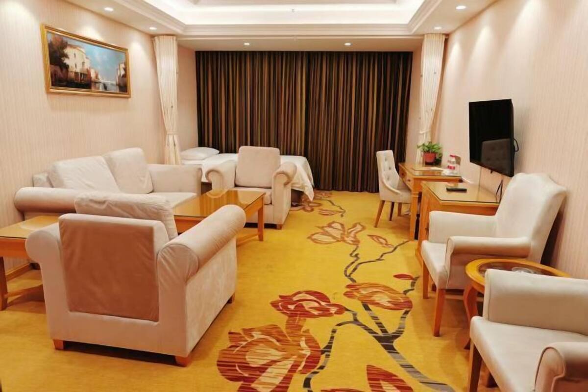 A hotel room with a sofa set, a dining table, a TV, and a carpet with floral patterns.