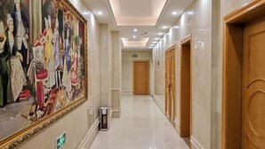 A hotel corridor with a large classical painting on the left, wooden doors on the right, and a clean, tiled floor. - Vienna Hotel ( Liaocheng Tita Jinding Shopping Center Branch) (Liaocheng)