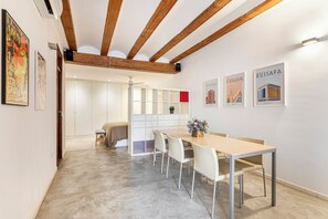 A modern dining area with a wooden ceiling, white walls, and a long table with chairs. There are framed pictures on the wall and a plant on the table. - Loft Market Mossen Sorell (Valencia)