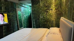 Una cama con sábanas blancas, un televisor a la izquierda y una pared con diseño similar al bambú.