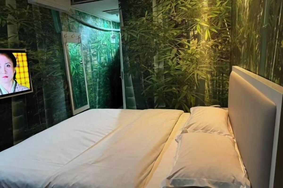 A bed with white linens, a television on the left, and a wall with a bamboo-like design.