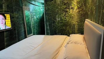 Uma cama com lençóis brancos, uma televisão à esquerda e uma parede com design semelhante a bambu.