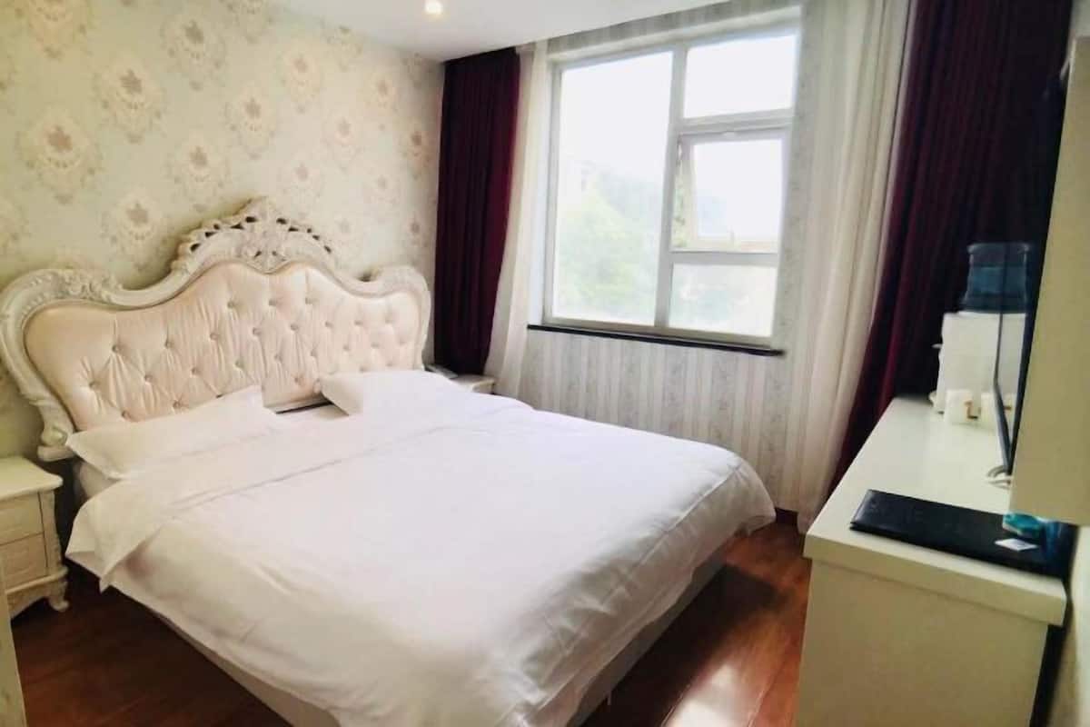 A neatly made bed with a headboard, a bedside table with a lamp, and a window with curtains.