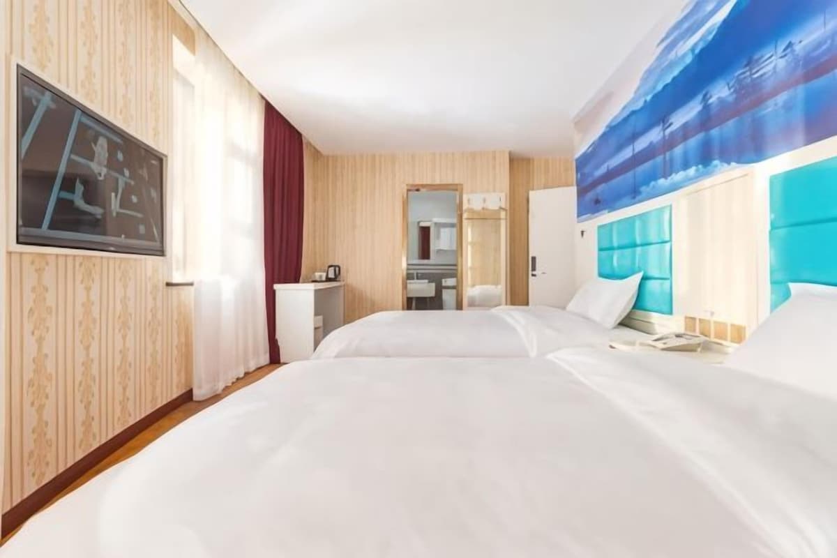 A hotel room with a large bed, a desk, a mirror, and a bathroom visible through an open door.
