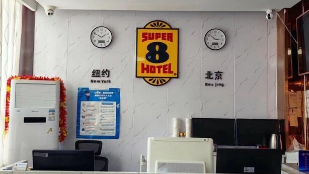 A hotel reception area with a 'Super 8 Hotel' sign, two clocks, a computer, a printer, and a bulletin board. - Super 8 Hotel (Beijing You'anmen Outer Street) (Beijing)