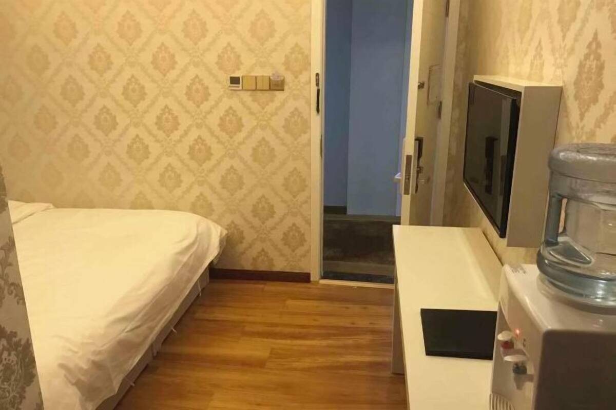 A hotel room with a bed, a television, a water dispenser, and a patterned wall.
