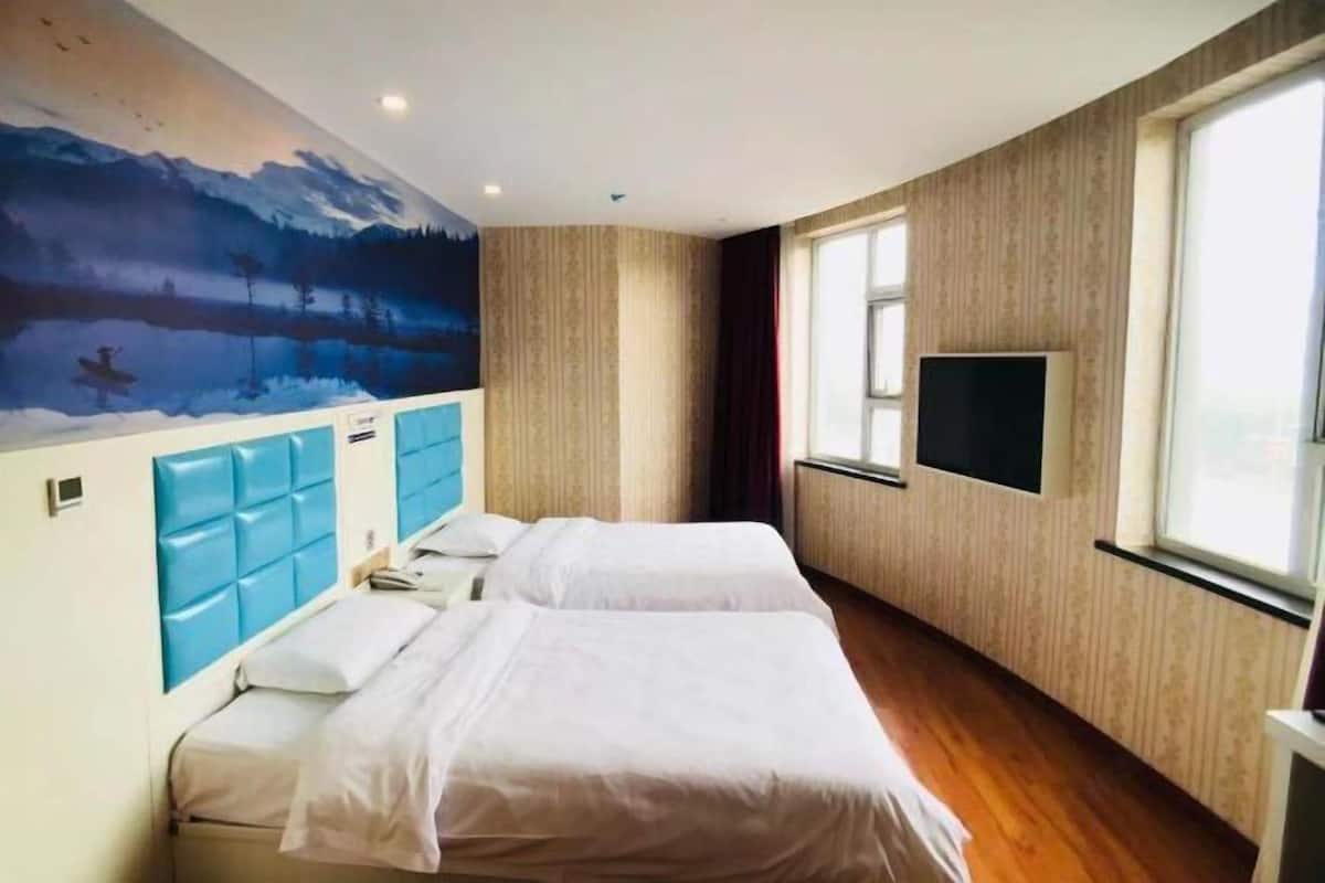 A hotel room with two beds, a large window, a mounted TV, and a mural on the wall.