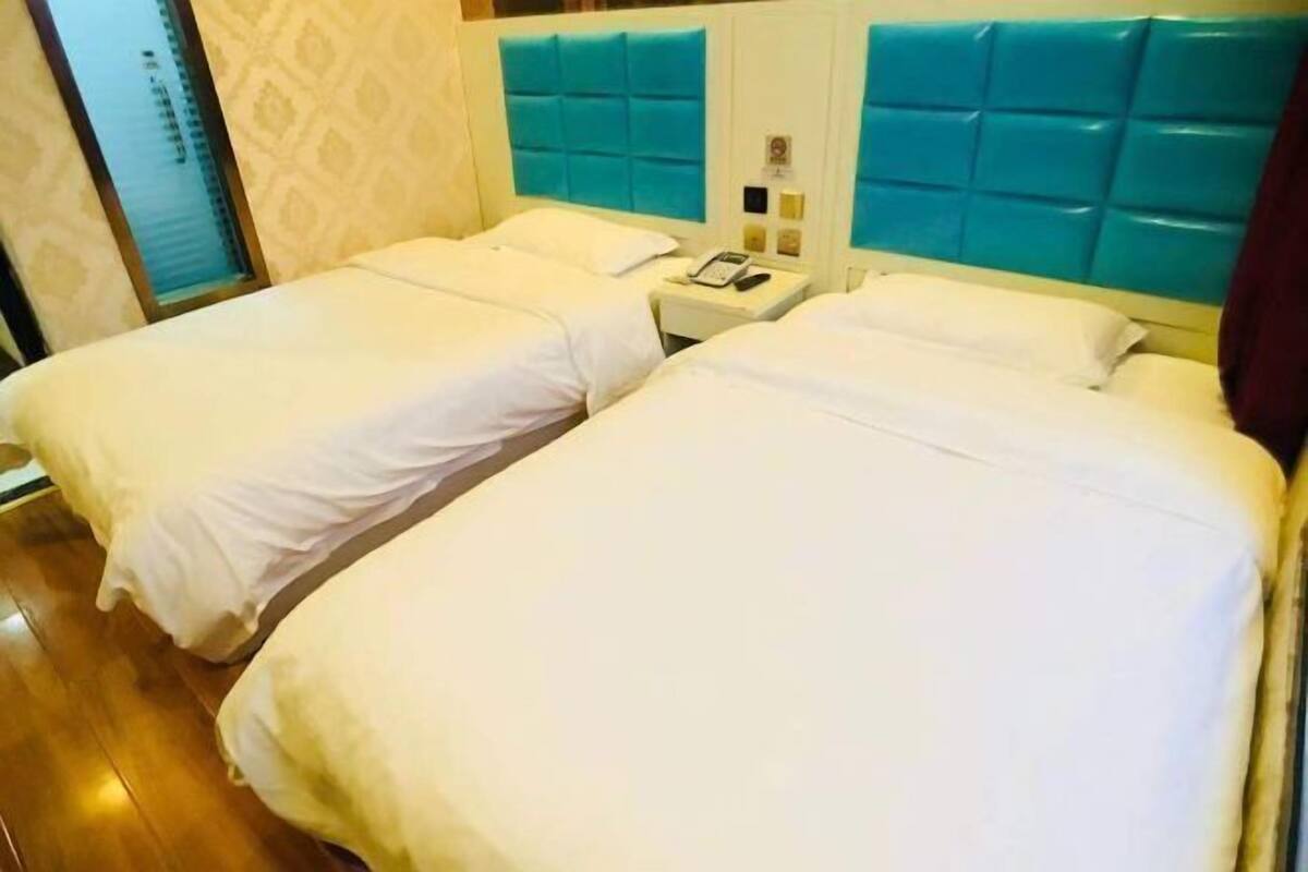 A hotel room with two single beds, a nightstand with a phone, and a wall-mounted control panel.