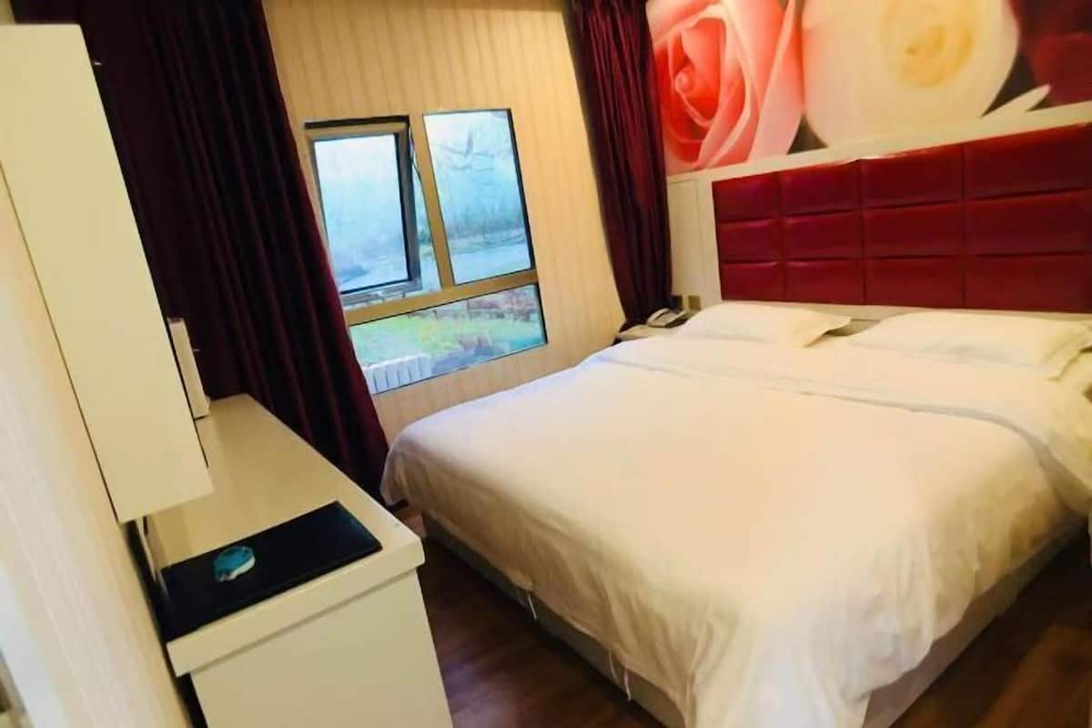 A bedroom with a bed, a window, a desk, and a red headboard.