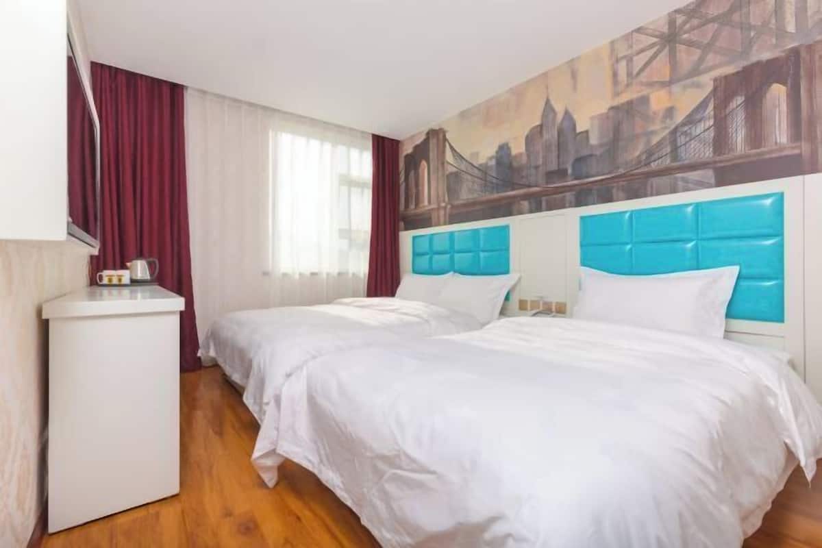 A hotel room with two beds, a white headboard, a small white table, and a cityscape mural on the wall.