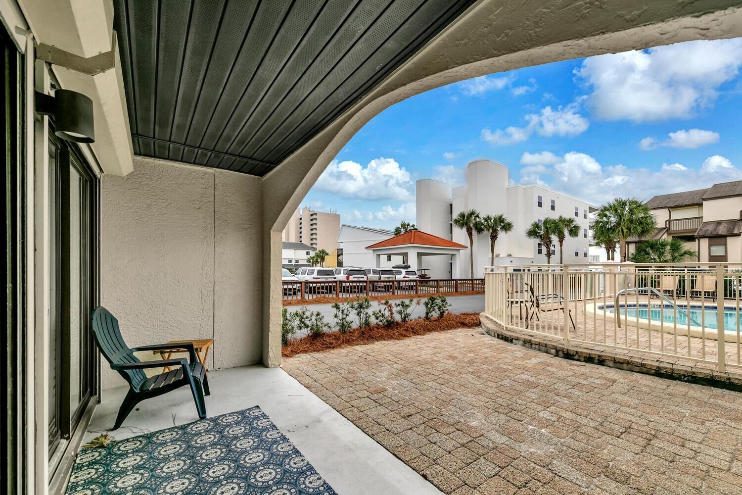 Un balcón con piscina, una silla y vistas a edificios y palmeras.